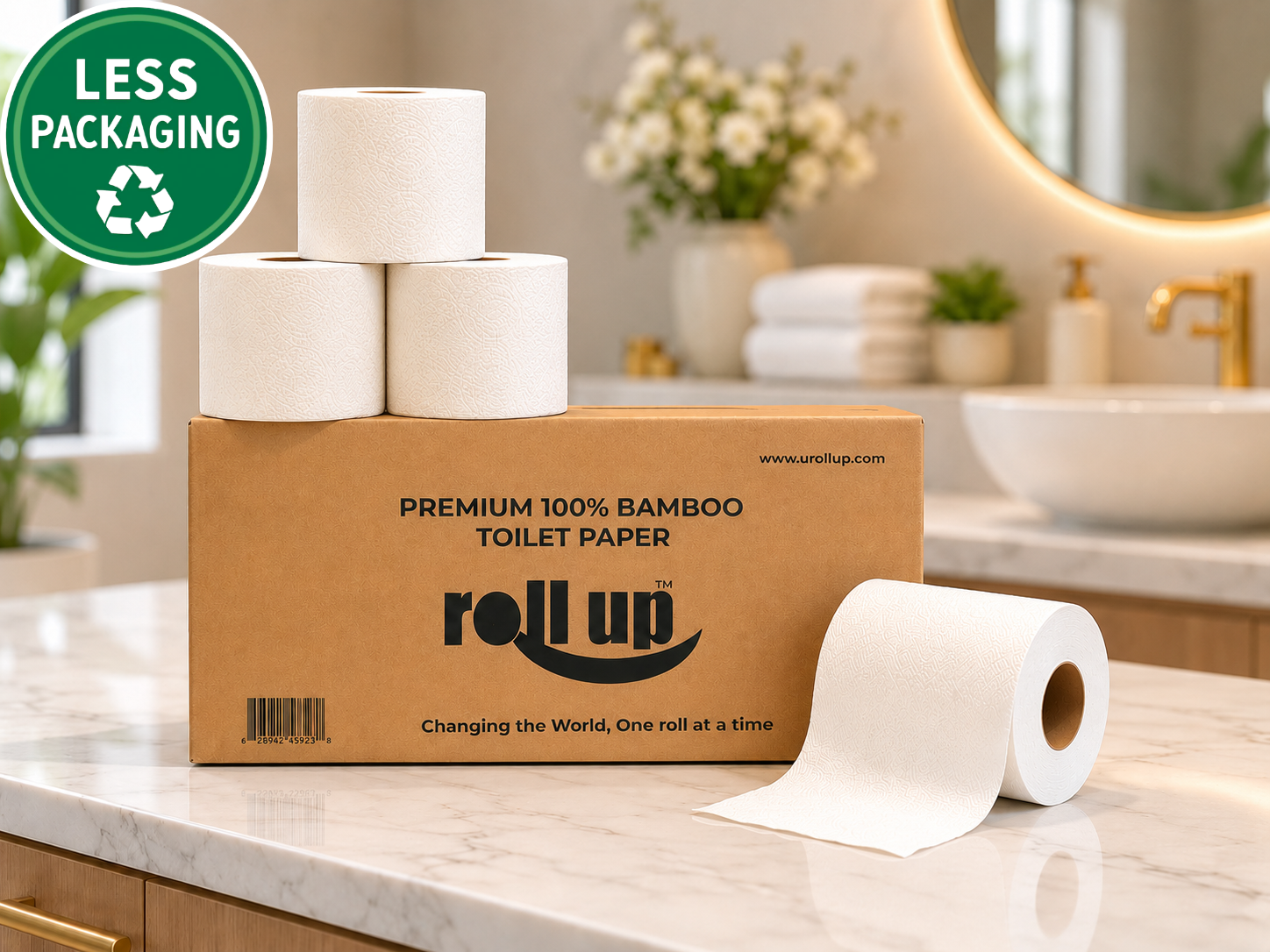A box of Roll Up premium 100% bamboo toilet paper with four rolls stacked on top and one unrolled in front, set on a marble bathroom counter with a sink and mirror in the background. A green circular badge in the top-left says 'LESS PACKAGING'.